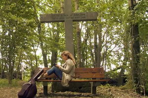 Frau sitzt auf Bank vor Kreuz