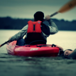 Junge im Kanu zieht Mann aus Wasser