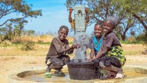 Drei Jungen spielen mit dem sauberen Wasser am Brunnen.