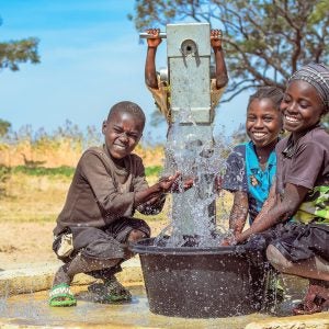 Drei Jungen spielen mit dem sauberen Wasser am Brunnen.