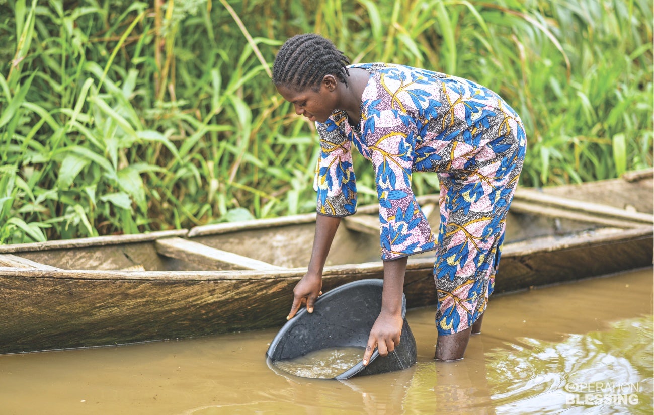 Eine nigerianische Frau schöpft Wasser aus einem verunreinigten Fluss