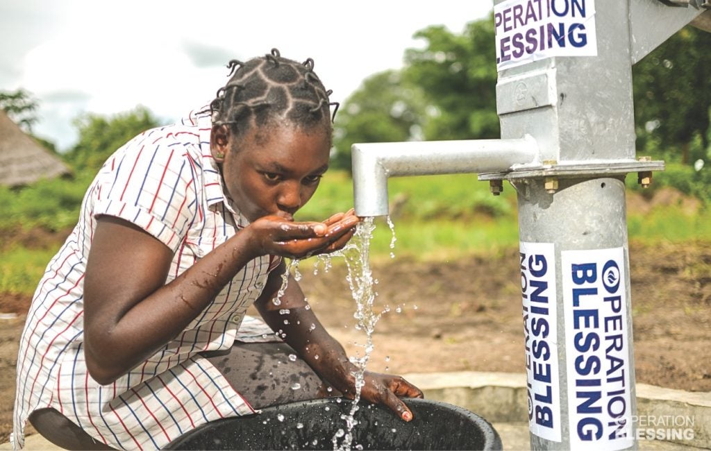 Eine nigerianische Frau trinkt Wasser aus einem Brunnen