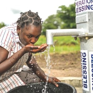 Eine nigerianische Frau trinkt Wasser aus einem Brunnen
