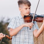 Zwei jungen stehen in einem Feld und spielen Geige