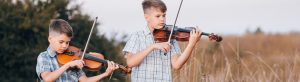 Zwei jungen stehen in einem Feld und spielen Geige