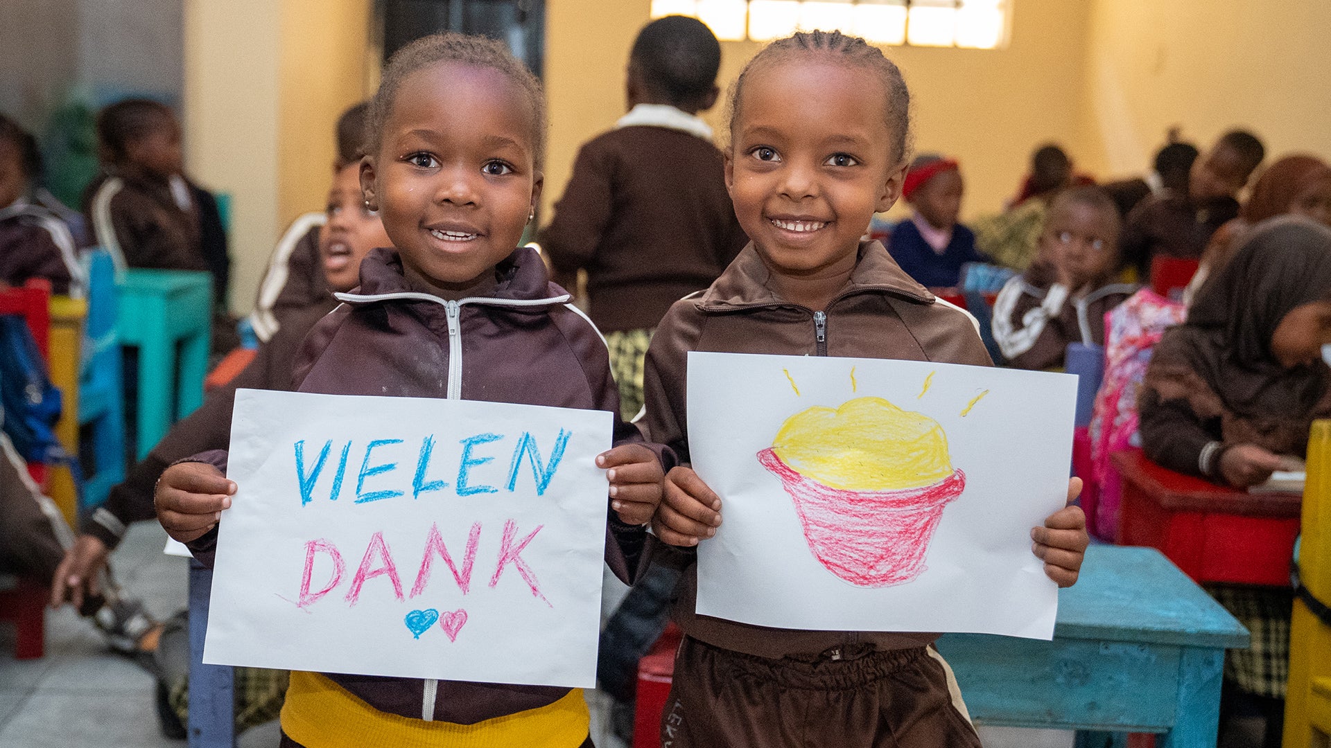 vielen-dank-aus-kenia Zwei Schülerinnen einer von CBN unterstützten Schule halten selbstgemalte Bilder mit einer Schüssel Essen und einem "Vielen Dank" hoch.